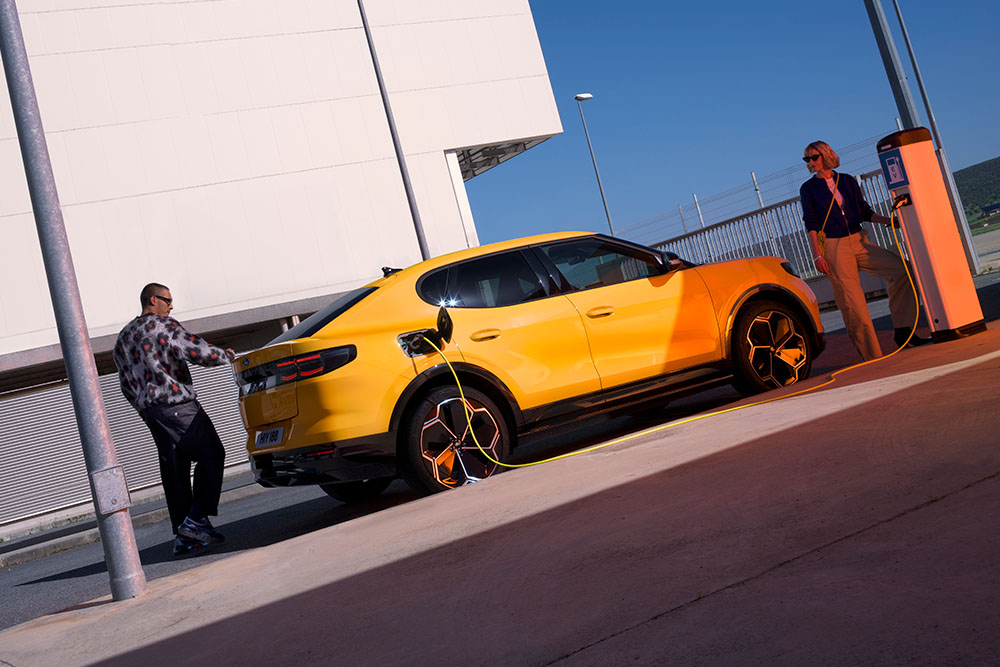 Un Capri 100% électrique jaune à une station de recharge. Un homme et une femme se tiennent près de la voiture.