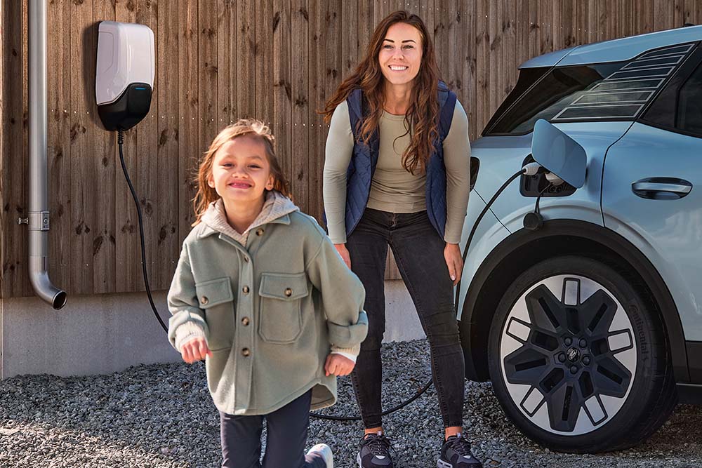 Une femme et son enfant rient tandis qu’un véhicule électrique  Ford se recharge derrière eux.