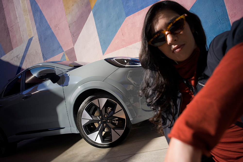 Une personne assise à côté d'une voiture Mild Hybrid Ford Puma gris.
