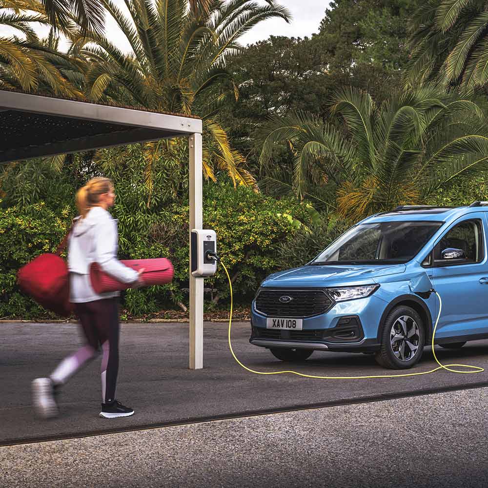 Une personne avec un tapis de yoga se dirigeant vers un fourgon Plug-in Hybrid Ford Tourneo Connect.