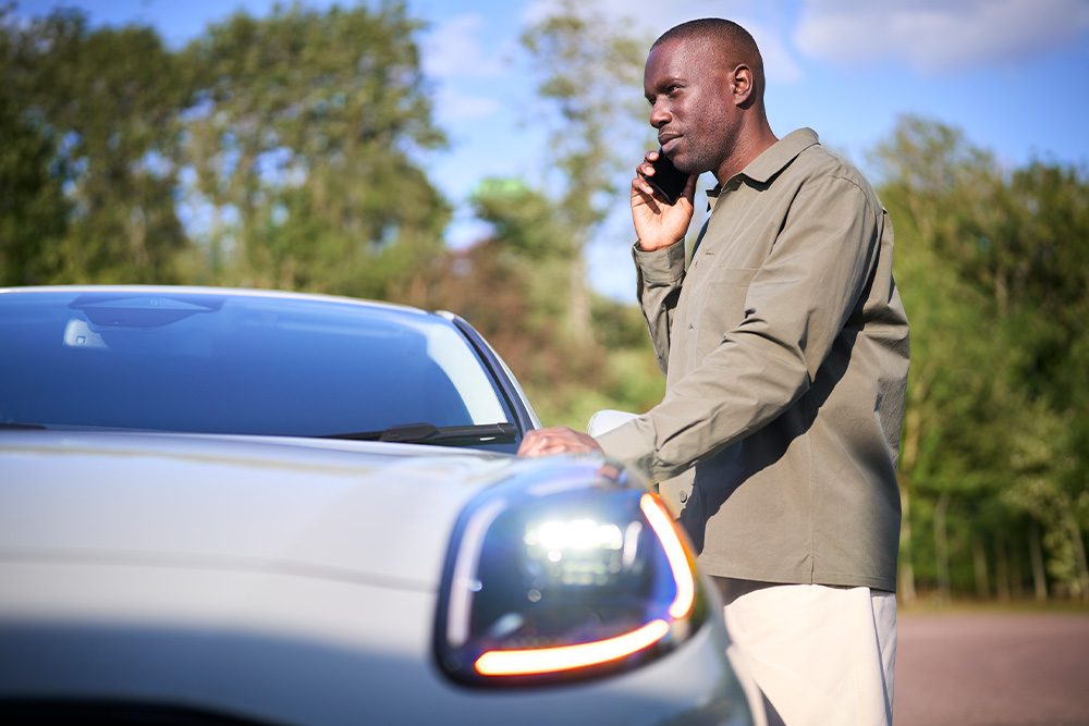Un homme parle au téléphone, appuyé sur le capot d'un Ford Puma blanc.