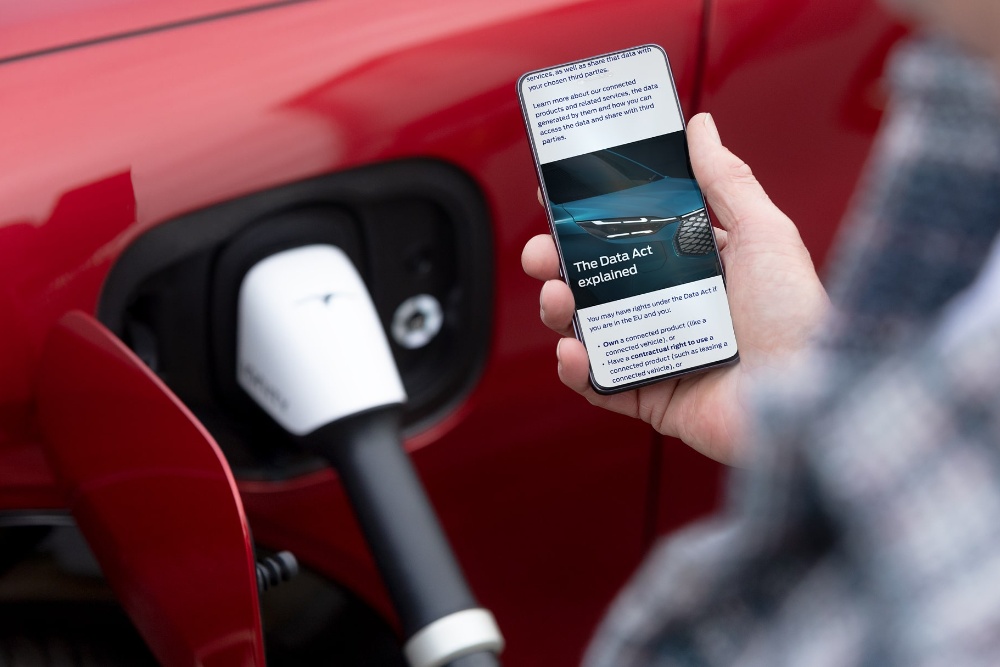 Une personne lisant une explication du Règlement européen sur les données sur son téléphone, à côté d’un véhicule électrique en charge.