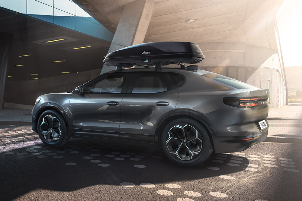 Vue 3/4 latérale d'un Ford Capri rouge avec un coffre de toit, garé sous une structure de bâtiment moderne.