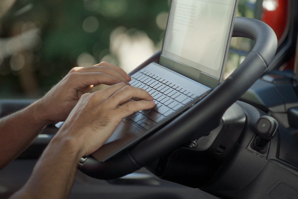 Les mains d'une personne tapent sur le clavier d'un ordinateur portable sur le volant rabattu à plat du Ford Tourneo Custom.