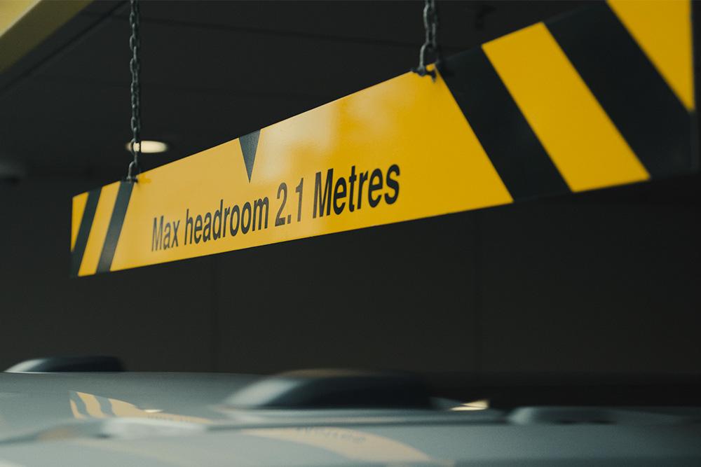 Panneau jaune et noir dans un parking couvert indiquant « Hauteur maximale 2,1 mètres ».