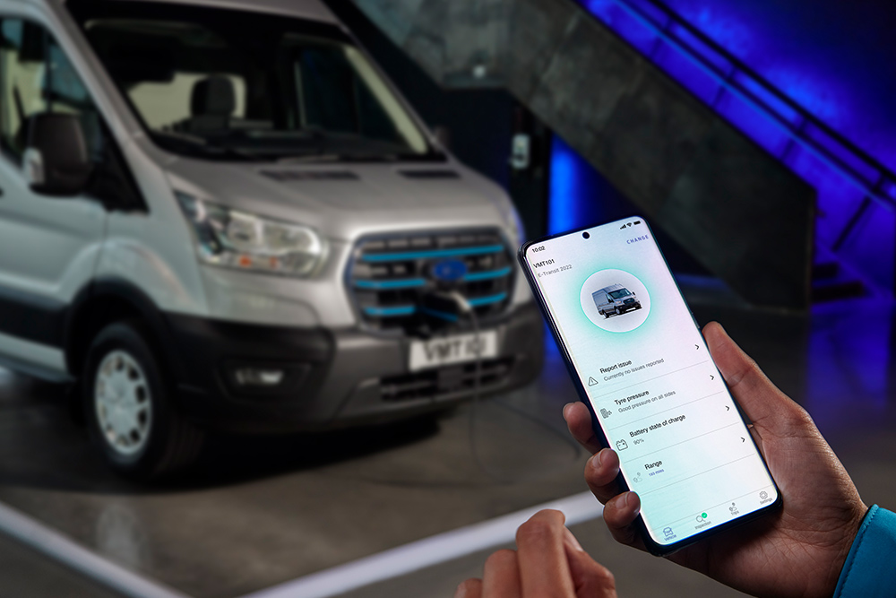 Téléphone affichant l’écran Ford apps, avec un fourgon Ford E-Transit en cours de recharge à l’arrière-plan. 