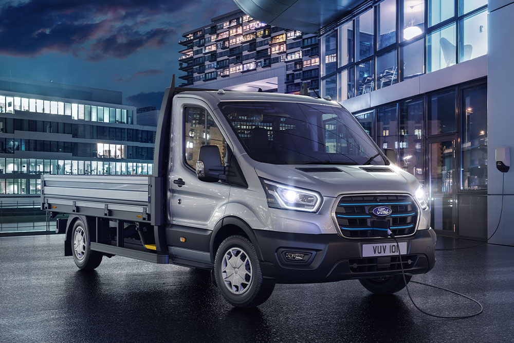 Ford E-Transit châssis-cabine argenté stationné devant un bâtiment moderne, de nuit.