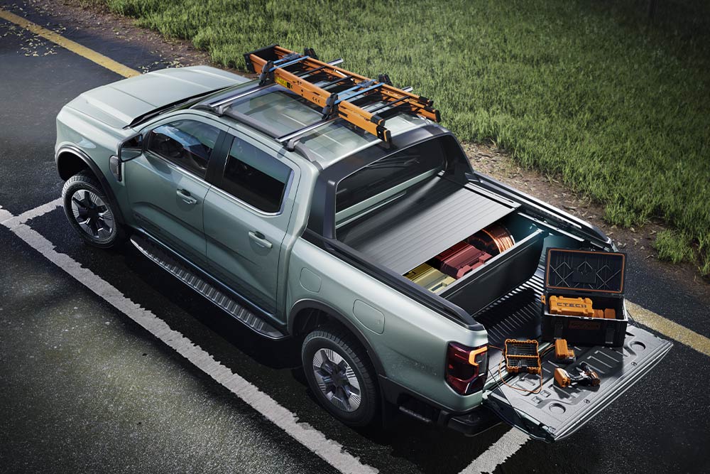 Vue arrière en plongée d'une camionnette Ford Ranger grise, benne ouverte avec outils et galerie de toit sur une surface pavée.